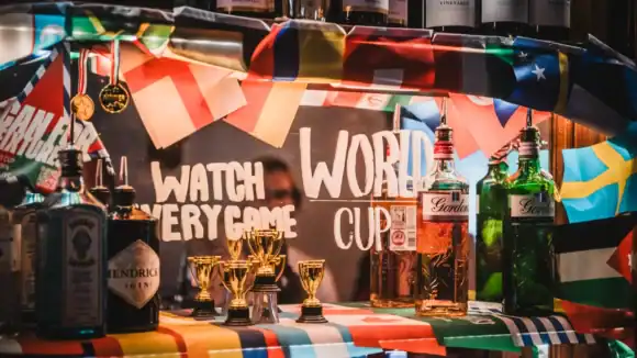 Bar setup with alcohol bottles, trophies, and flags for World Cup celebration.