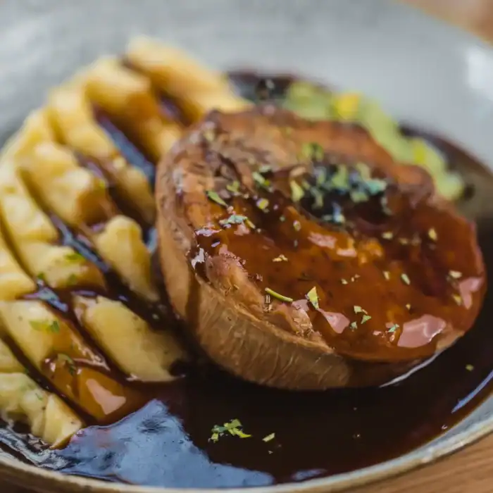 Gourmet dish with mashed potatoes, mushroom, and rich gravy on a ceramic plate.