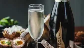 Champagne bottle with glass of bubbly and assorted food on table.