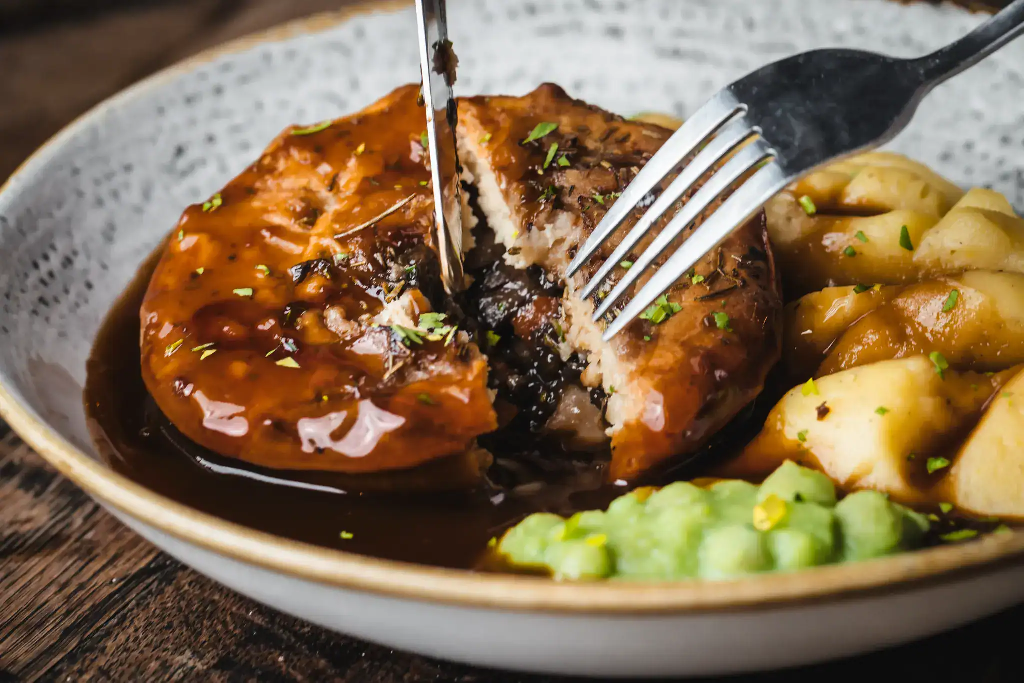 Close-up of a hearty meat pie with gravy, served with potatoes and vegetables.