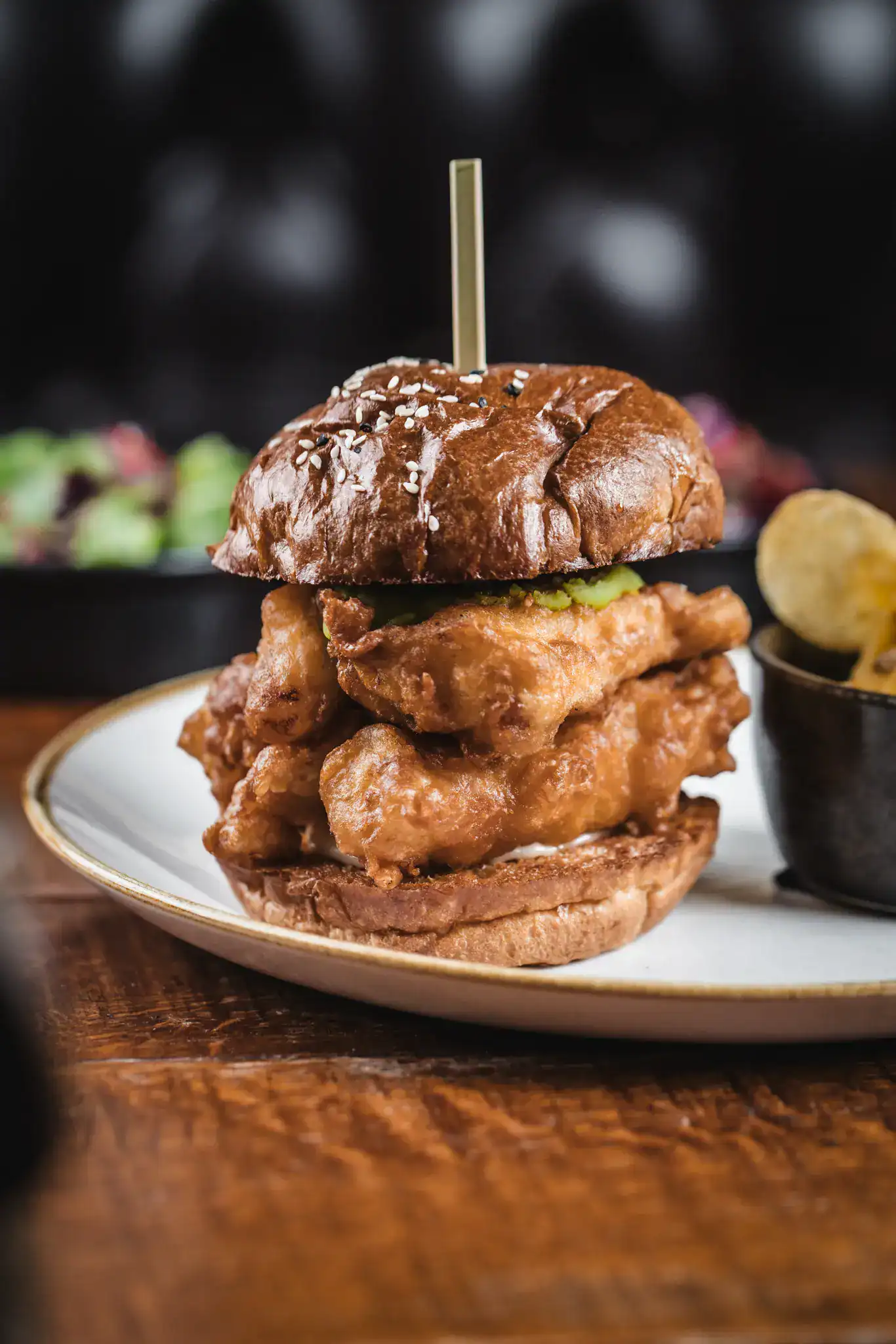 Delicious burger with fried chicken, pickles, and bun on a white plate.