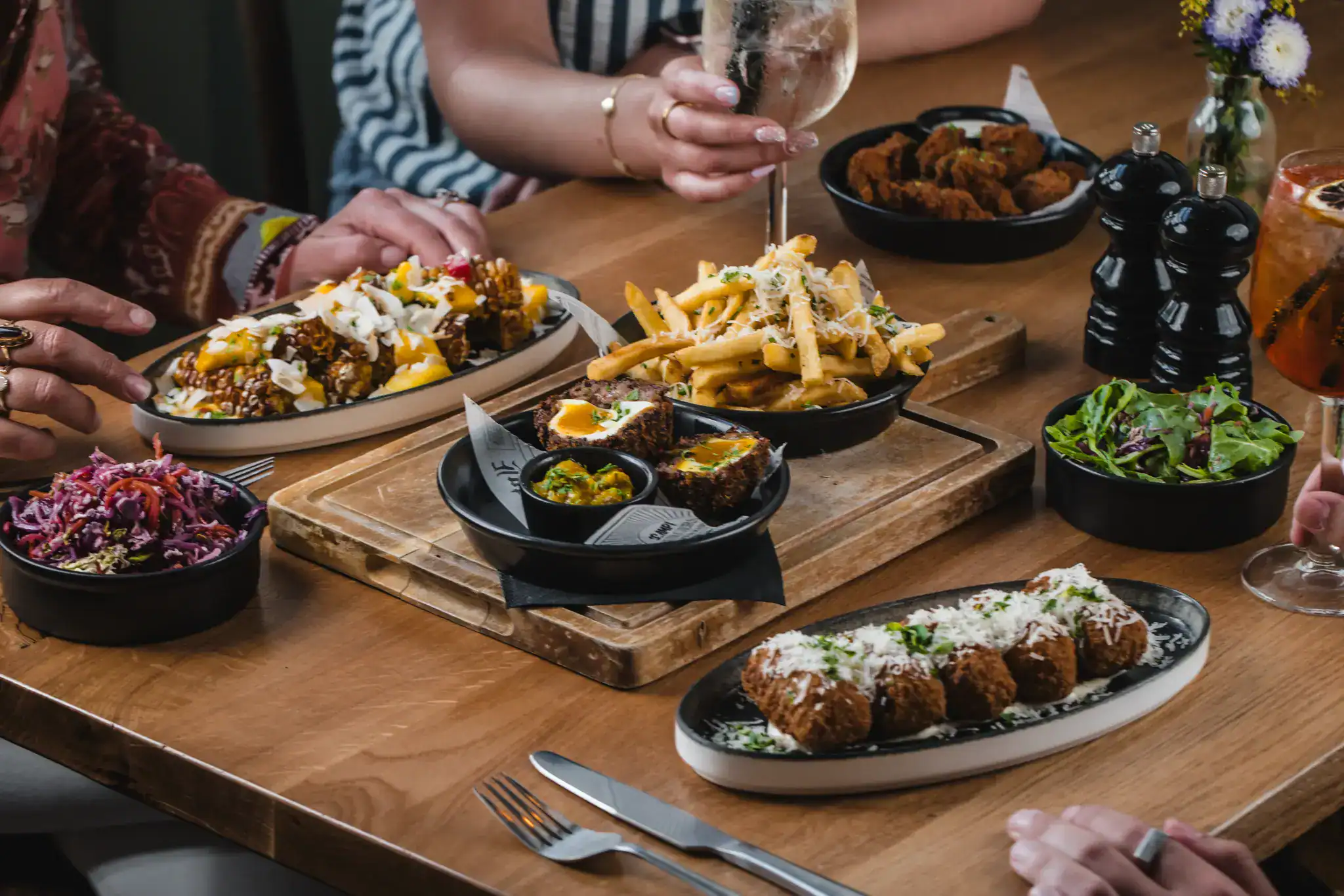 Assorted gourmet dishes including fries, fried chicken, and salads on a wooden table.