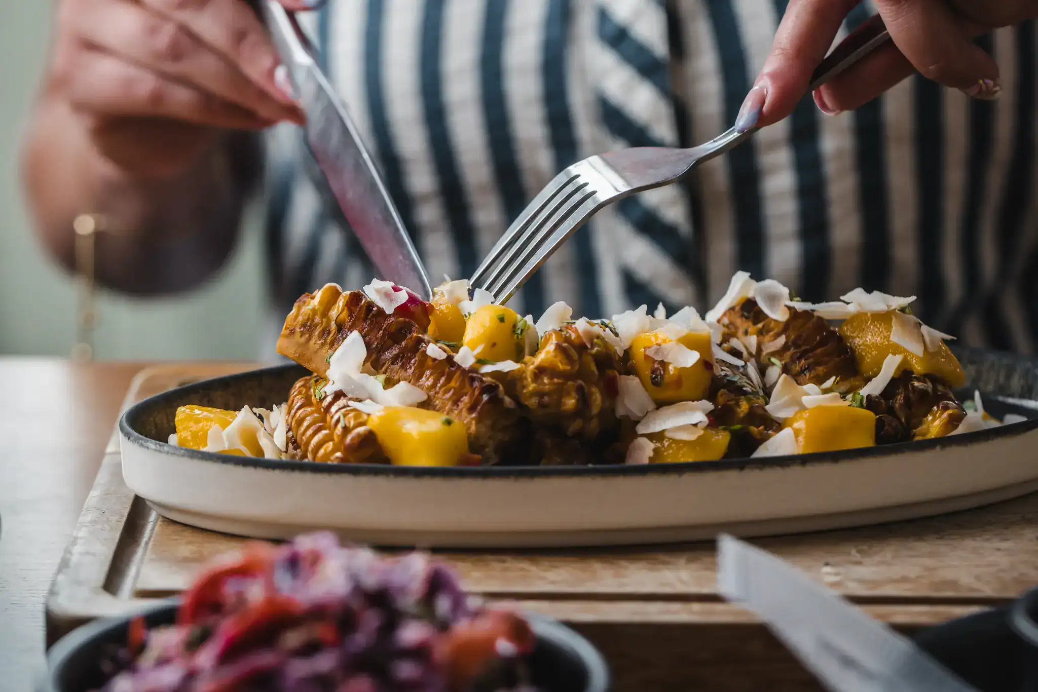 Person eating a dessert with meat, mango, and whipped cream.