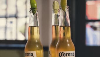 Three Corona Extra beer bottles with lime wedges on a wooden table.