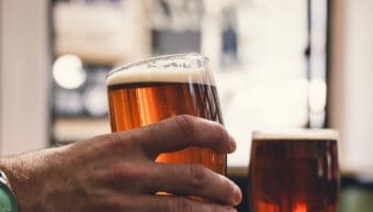 Person holding a pint of amber beer in a pub setting.